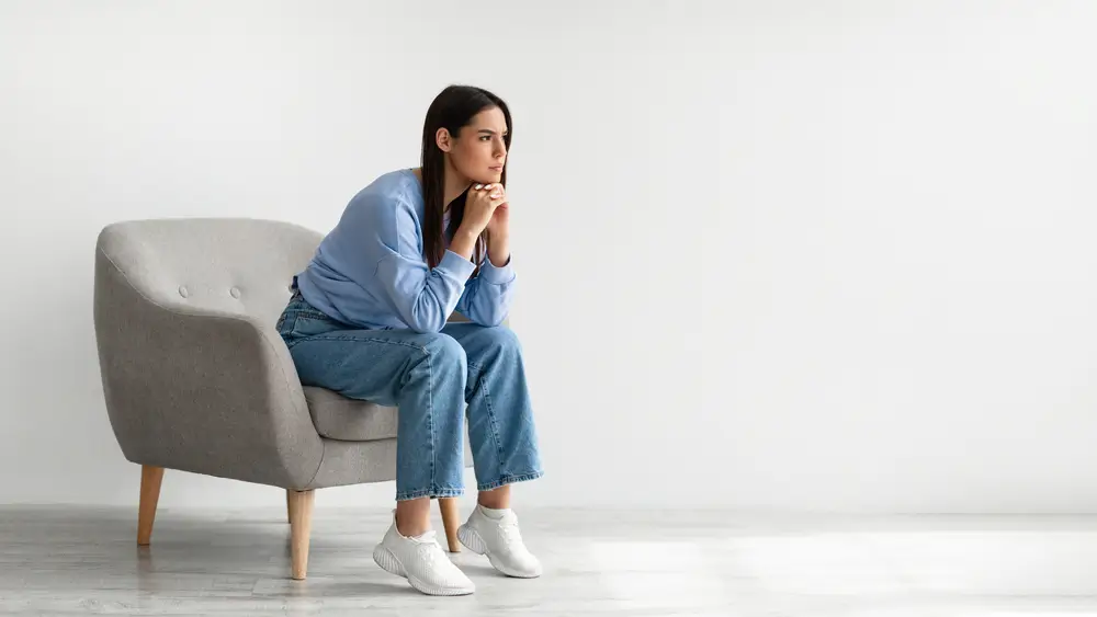 Portrait d'une jeune femme agacée assise dans un fauteuil contre un mur blanc de studio, dessin de bannière avec espace libre.