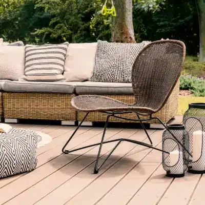 Patterned pouf and rattan chair on wooden patio with pillows on sofa and lanterns.