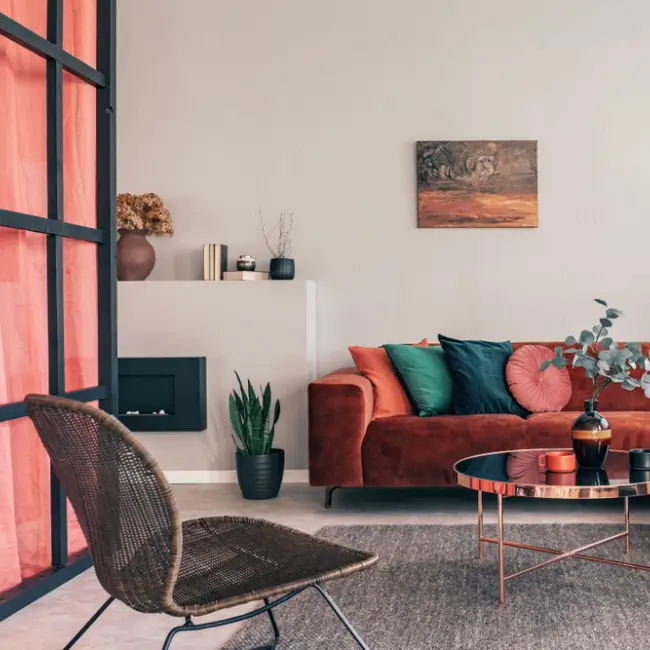 Photo réelle d'un intérieur de salon confortable avec une table ronde sur un tapis gris, un fauteuil en osier et un canapé d'angle rouge.