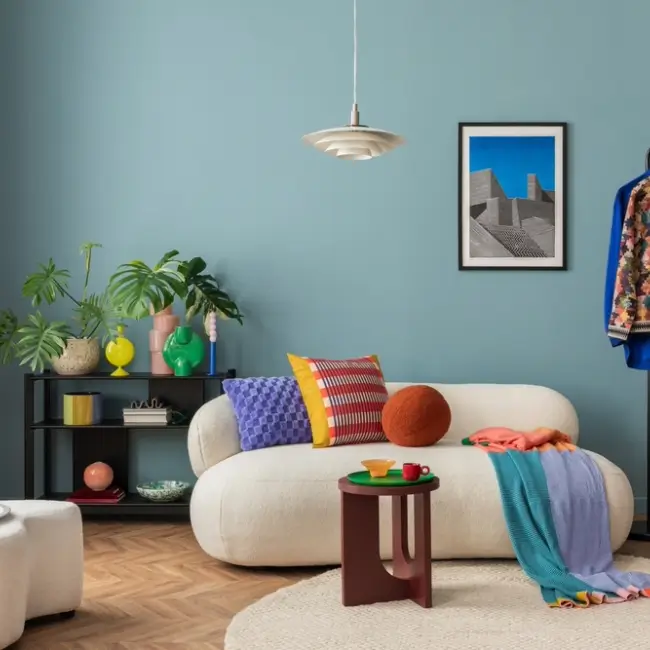 Intérieur moderne et coloré d'un salon avec canapé design en bouclette, poster décoratif, étagère, plantes, décorations et objets personnels.