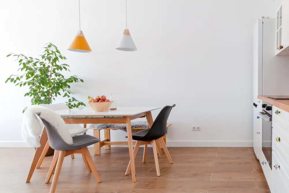 Intérieur moderne de cuisine confortable, salle à manger, mobilier blanc, lampes au-dessus d'une table en bois, chaises, pommes, bowl.